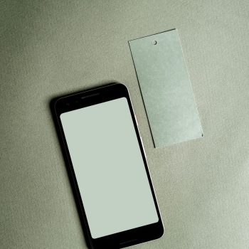 A smartphone with a blank screen alongside a tag on a green fabric surface. Perfect for mockup designs.